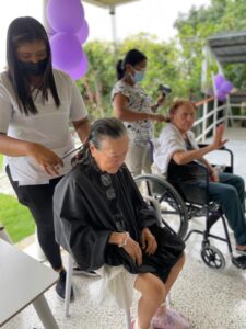 Residente disfrutando de un secado de cabello mientras conversa con la cuidadora.