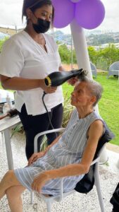 Residente disfrutando de un secado de cabello mientras conversa con la cuidadora.