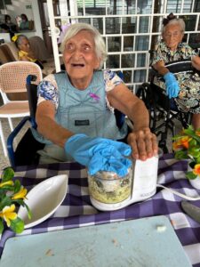 Residente mezclando ingredientes mientras conversa con la cuidadora.